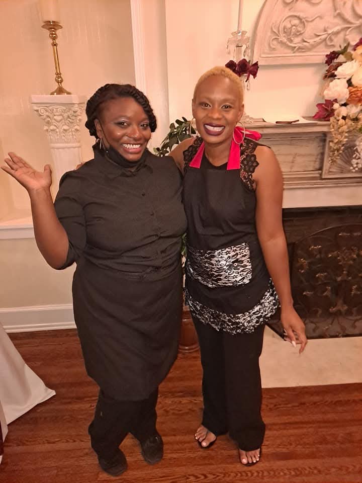 Two servers welcoming guests beside a decorated fireplace